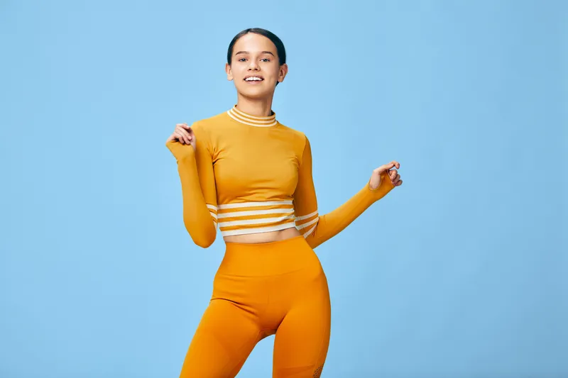Fitness woman in bright orange athletic wear poses confidently against a blue studio backdrop, showcasing athletic woman movement and energy for exercise, workout and active lifestyle visuals.
