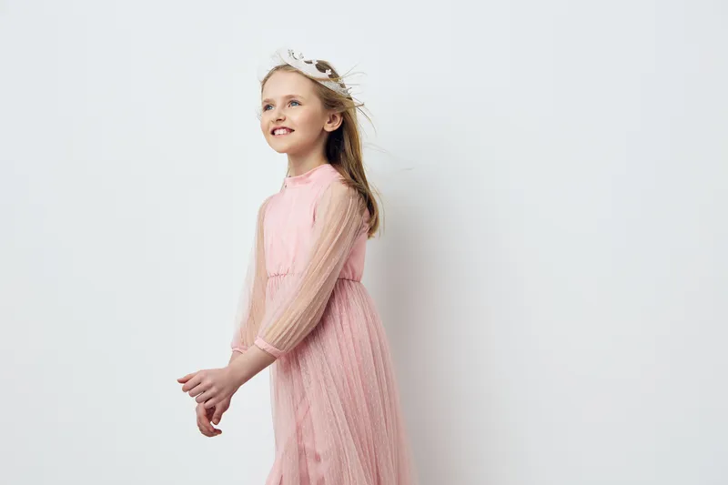 Young girl in a pink dress smiling joyfully against a simple white background, highlighting childhood innocence and playful elegance