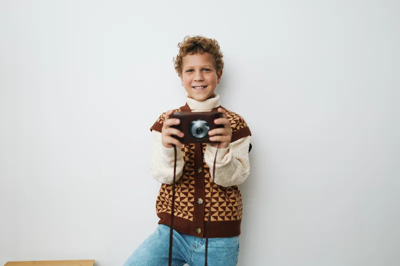 An authentic moment of a young student photographer holding a camera, showcasing a candid school life scene and a playful game spirit. Joyful curiosity and daily routine.
