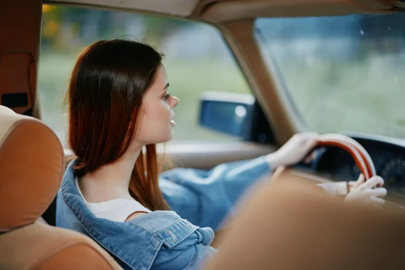 Young woman driving a car, wearing a denim jacket, with a thoughtful expression on her face, capturing a moment of tranquility and freedom.
