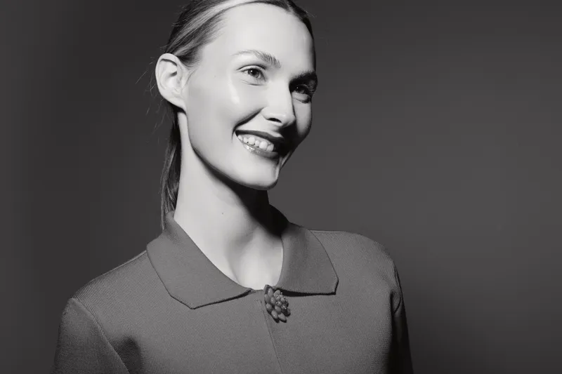 Smiling Caucasian woman with light skin and tied back hair wears textured sweater, looking away in studio with dark background. Concept of happiness and natural beauty.