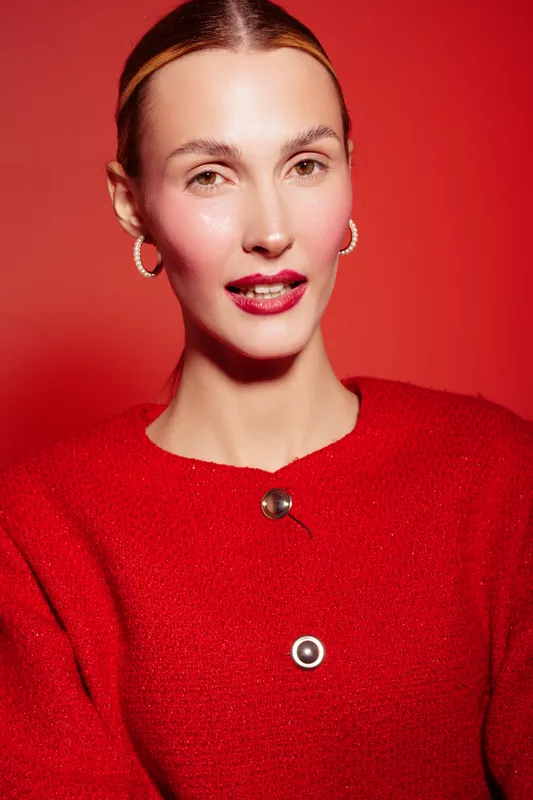 Portrait of a young woman with slicked back hair wearing red sweater and hoop earrings on red background. Concept of fashion, beauty, and confident female model.
