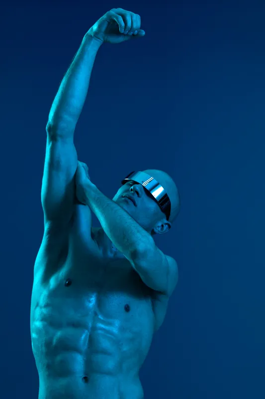 Athletic man showcasing strength in a dynamic pose, highlighting toned muscles and an expressive gesture. A striking blue light creates a captivating atmosphere.