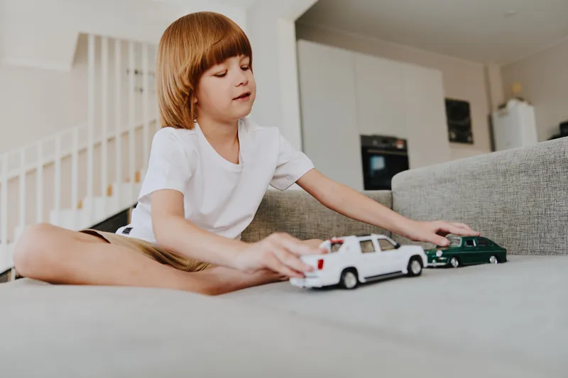 Engaged boy playing with toy cars on a soft couch, showcasing creativity and joy. The warm, inviting atmosphere enhances his imaginative playtime experience.