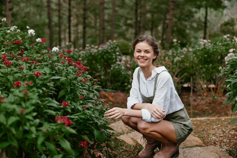 Smiling young woman in a casual outfit among blooming flowers in a sunny nature setting, embracing joy and beauty in the spring season