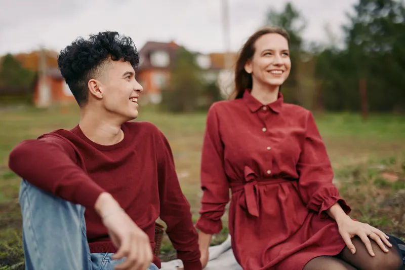 Two friends sit on a blanket in a park, sharing a candid moment that captures authenticity and genuine connection under warm autumn light and a calm, natural setting.