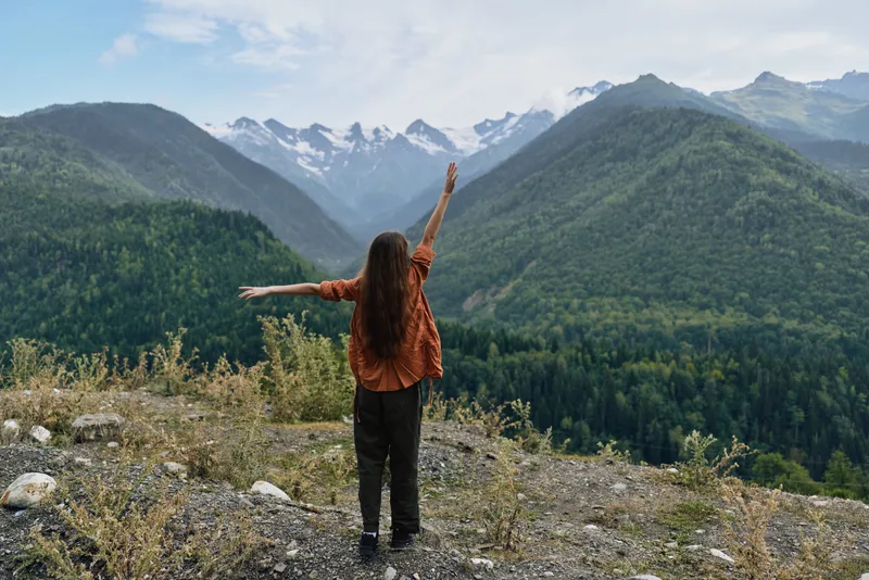 Person woman stands with arms raised on a mountain overlook, mountains nature freedom outdoor landscape hiking, authenticity and inclusivity in adventurous portrait