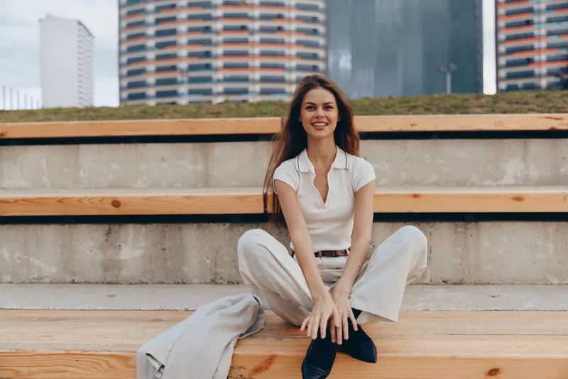smiling woman in casual white outfit sitting on wooden stairs urban background modern lifestyle fashion seasons
