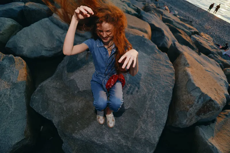 lifestyle woman in modern boho-western denim street style jumps joyfully on rocks with vibrant film color tones and natural outdoor light