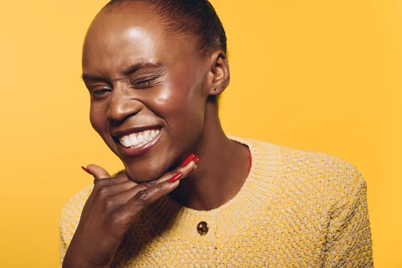 Smiling dark skinned African woman with natural skin and short hair poses confidently on yellow background wearing a knitted sweater. Concept of beauty, happiness and self expression.