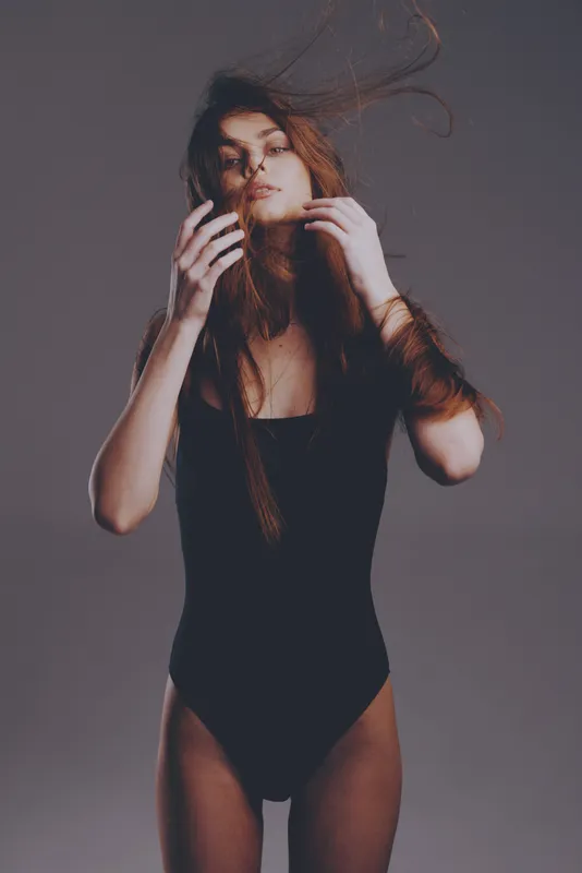 Woman posing in black bodysuit with flowing hair in studio, expressive and elegant mood