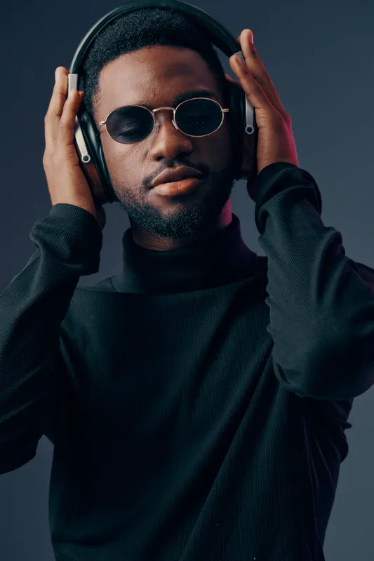 Stylish young man in sunglasses and headphones, enjoying music, with a moody background in dark tones, conveying feelings of relaxation and confidence