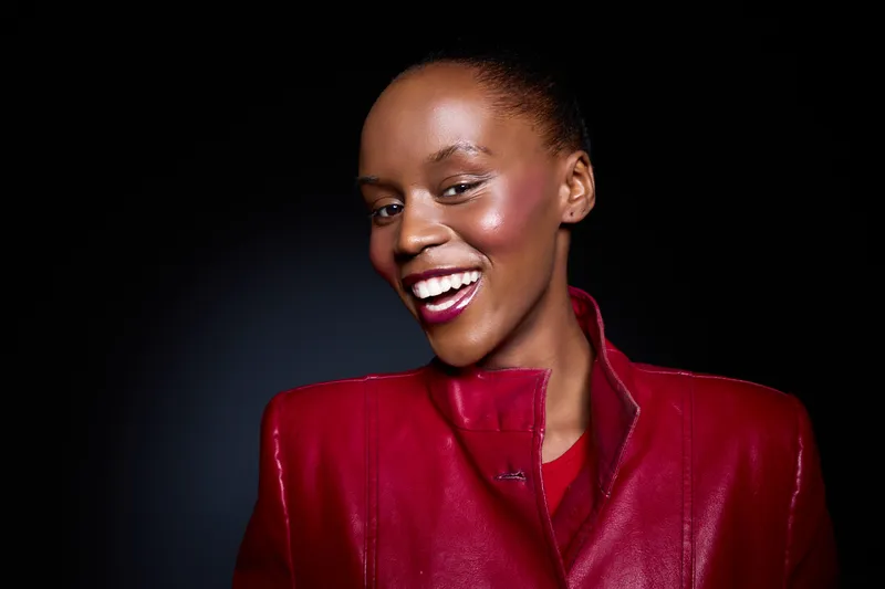 Confident African woman with dark skin smiling brightly, wearing a red leather jacket against a dark background. Concept for fashion, beauty, confidence, and empowerment.