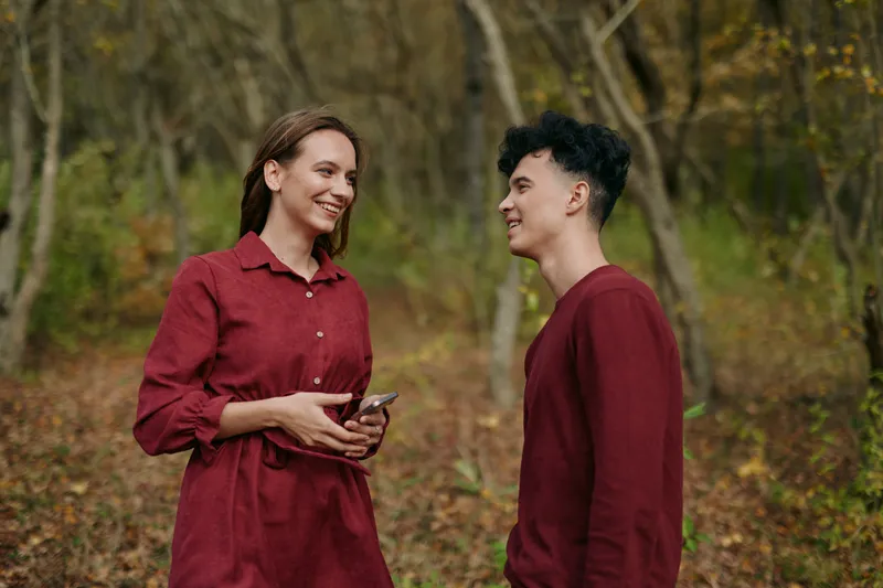 An authentic candid moment captures two individuals sharing a warm smile in a leafy autumn setting, a genuine, believable exchange amid rustic tones and natural light.