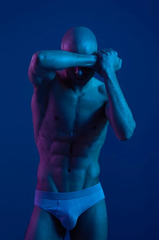Athletic man striking a dramatic pose in low light, showcasing toned muscles and expressions. Bold colors create a captivating and artistic atmosphere.