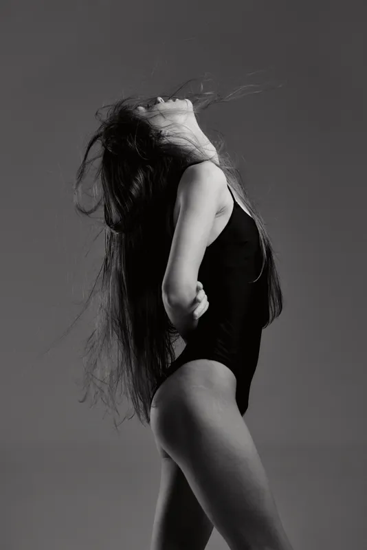 Black and white portrait of a slender woman in a black bodysuit with flowing hair and dramatic pose.