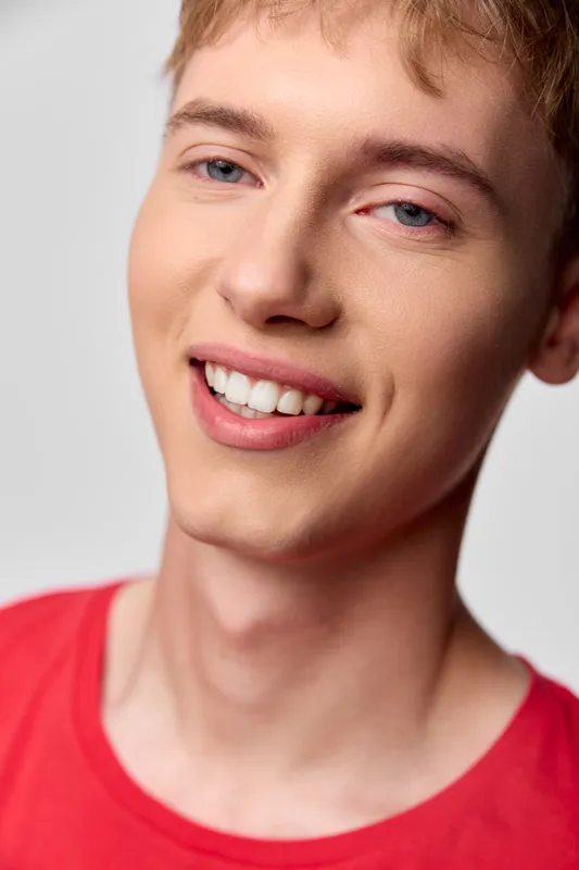 Closeup of a cheerful, young individual with a bright smile wearing a red shirt, conveying warmth, confidence and approachability for lifestyle, fashion and wellbeing contexts
