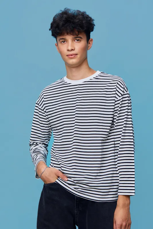 Young man wearing striped shirt stands confidently against blue background with relaxed posture and casual style, showcasing modern fashion and youthfulness.