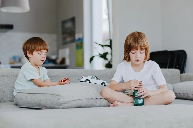 Two children playing together with toy cars in a cozy living room environment, showcasing joy and creativity through imaginative play.