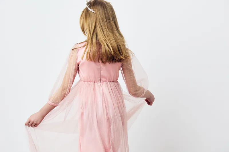 Charming young girl in a pink dress with sheer sleeves, conveying innocence and joy against a clean white background, perfect for children s fashion concepts