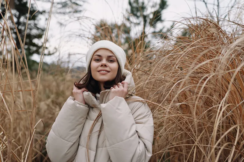 Winter outdoor portrait of a woman wearing a coat among tall grasses, muted natural light highlights a calm scene and cozy style in a serene outdoor setting.