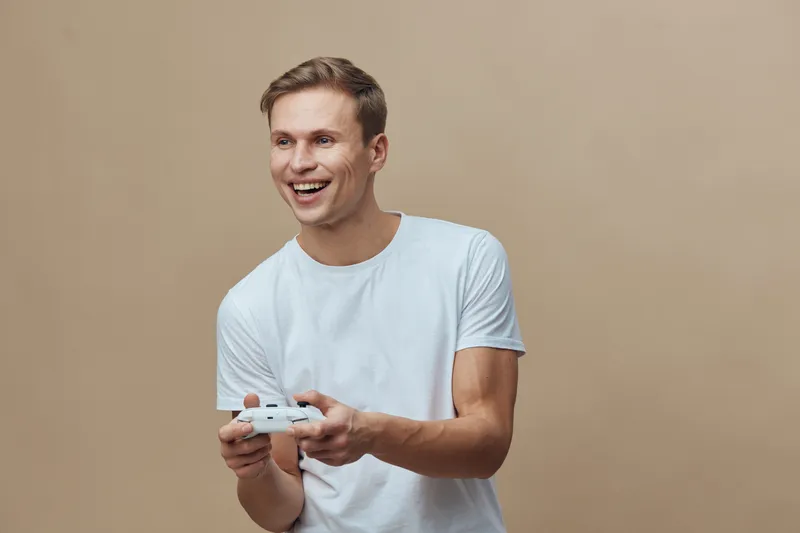 Smiling young caucasian man wearing white t-shirt play video game with wireless controller isolated on beige background digital entertainment leisure concept