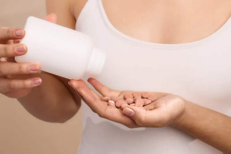 Asian woman pours pills from a bottle into her palm in a close up shot, conveying health care and wellness focus with a calm, clinical mood.