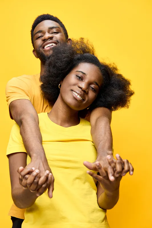 Joyful African couple in vibrant yellow matching outfits, embracing and smiling, showcasing love and connection against a bright yellow background