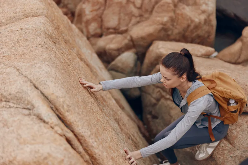 A determined young woman climbing a rocky surface during outdoor adventure, showcasing strength, perseverance, and nature s beauty in a vibrant outdoor setting