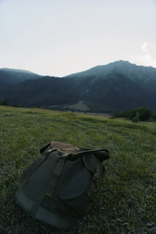 Backpack on a meadow with distant mountains, conveying outdoor travel, landscape, solitude, and a moment of quiet adventure in nature.
