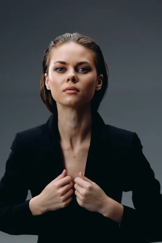 Confident woman in black jacket with intense gaze and dark background, portraying strength and elegance.