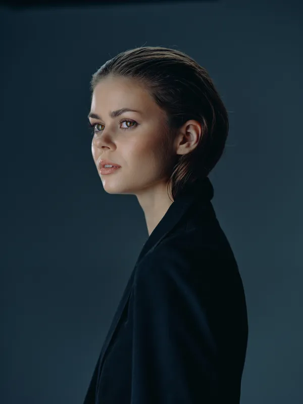 Profile of a young woman with freckles wearing a dark jacket against a neutral background, expressing calm and confidence