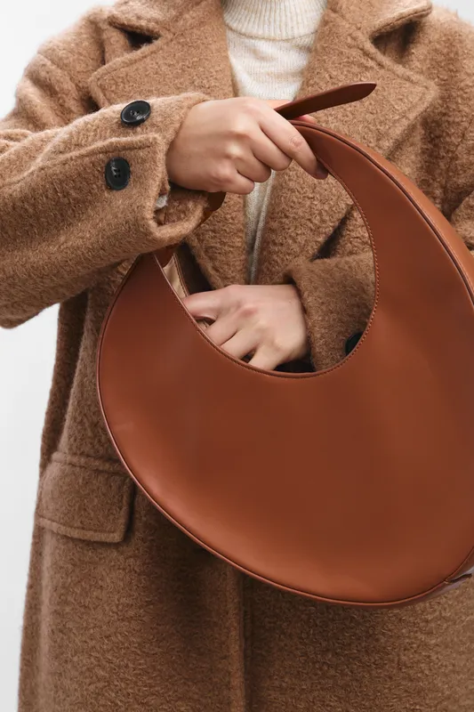 asian woman wearing a cozy brown coat holds a chic leather handbag, showcasing autumn fashion in a minimalist studio setting with neutral tones, capturing texture, warmth, and modern elegance for
