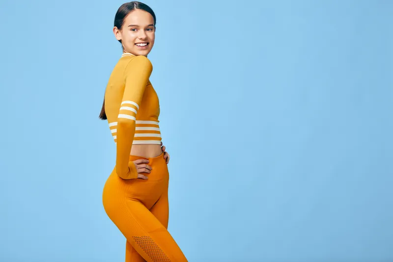 Young woman in bright orange athletic wear poses against a blue studio backdrop, exuding energy, fitness and confidence for sport, wellness, and active lifestyle projects.