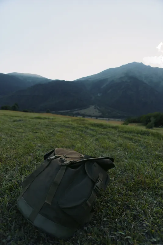 Backpack rests on a grassy field with distant mountains and clear sky, capturing a calm outdoor hiking moment and lone gear in a wide landscape