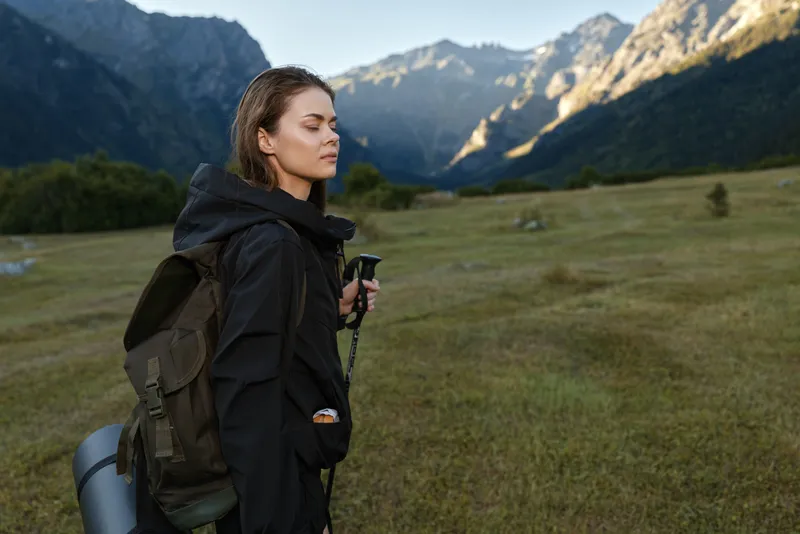A focused hiker stands in a misty mountain meadow, wearing a sturdy backpack and outdoor gear. She surveys rugged peaks, radiating calm confidence and adventurous spirit.