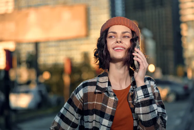 Woman on phone with smile in an urban golden light, candid lifestyle portrait showing authenticity and mindful living, warm autumn glow and emotional storytelling in city street.