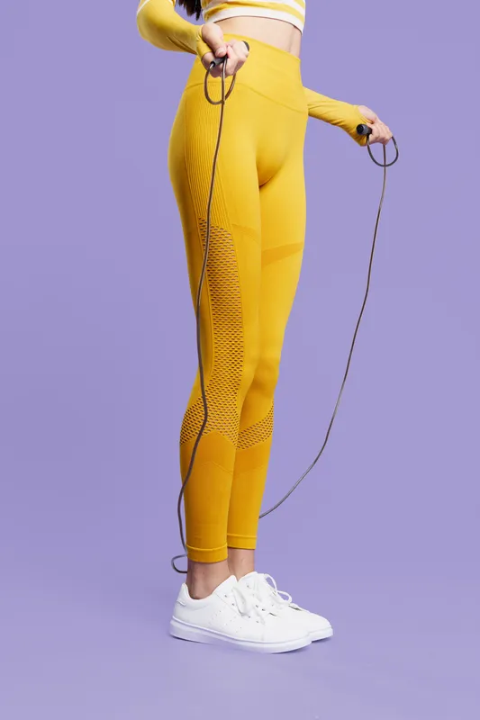woman sport fitness in yellow activewear holding jump rope, demonstrating healthy lifestyle, exercise focus, energetic mood, purple background