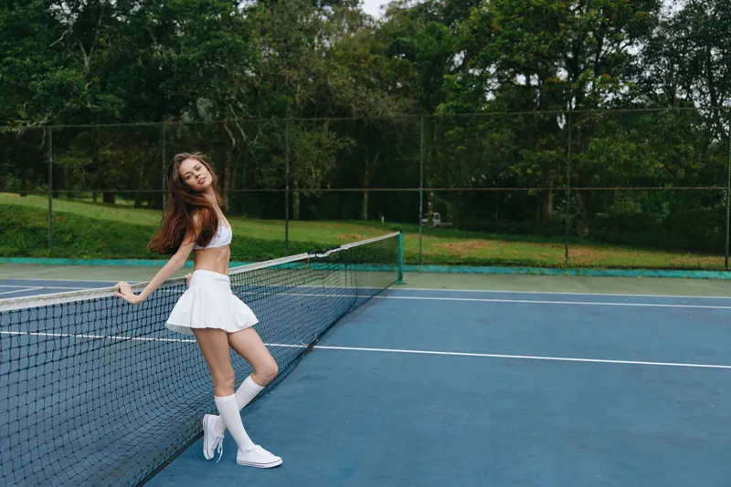 Young female tennis player enjoying a sunny day on the court, wearing white sports attire and demonstrating joy, perfect for promoting an active lifestyle