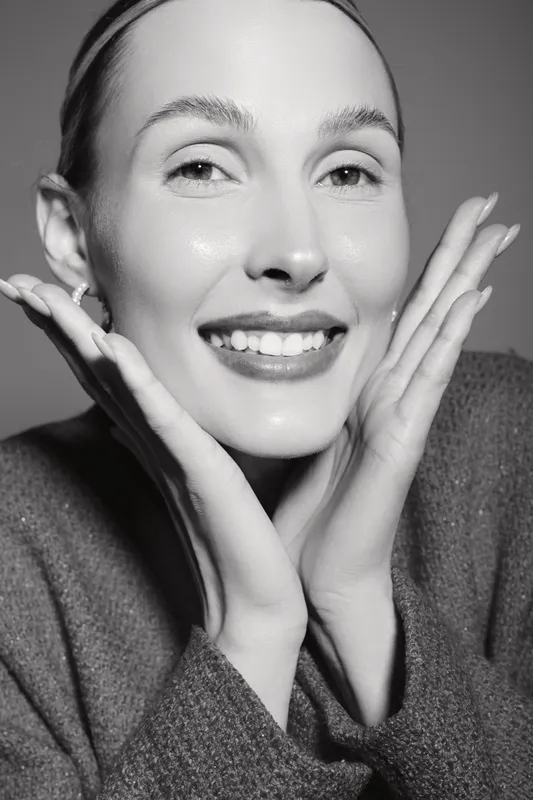 Close-up of a smiling Caucasian woman with fair skin touching her face with both hands. Portrait in soft lighting shows natural beauty, skincare, and positive mood concept.