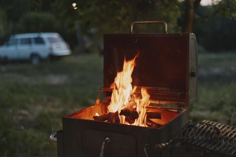 Cozy outdoor barbecue with flames, grill, and glowing embers at dusk, surrounded by nature, for summer gatherings and social events
