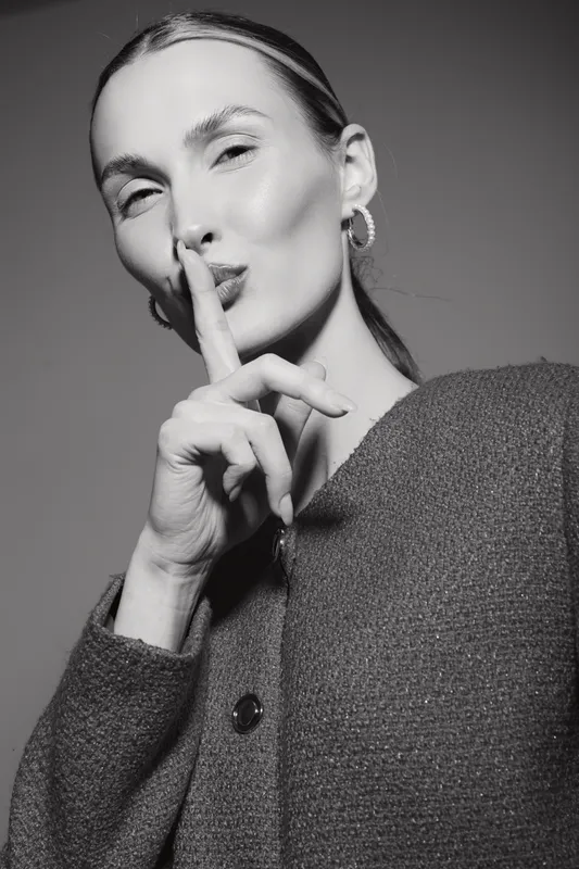 White woman with light skin makes silence gesture with finger on lips in studio monochrome portrait.