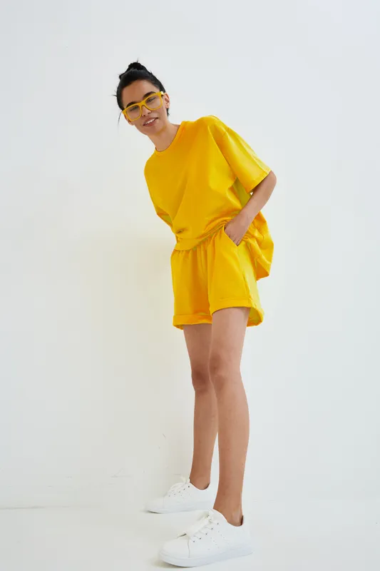 young woman wearing bright yellow casual outfit and white sneakers posing with hands in pockets against plain background, modern style and cheerful mood