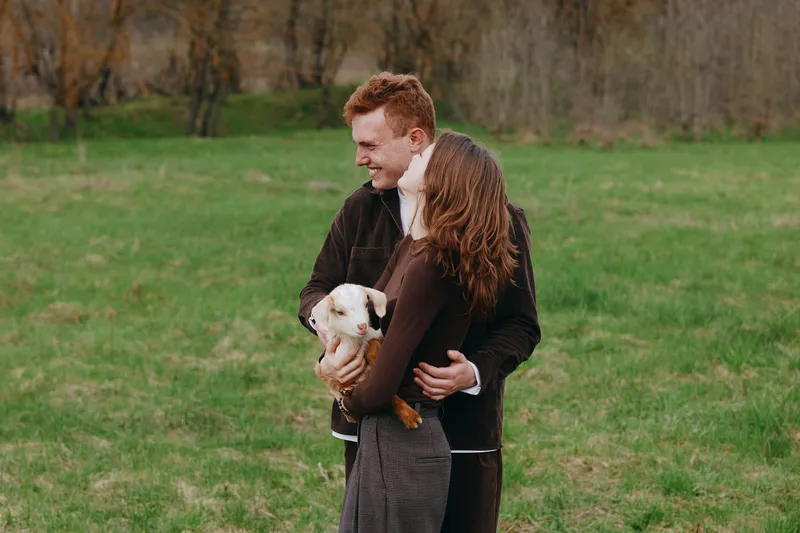 A smiling couple embraces with a dog in a green park, capturing a warm moment of love, companionship, and everyday happiness in a casual lifestyle scene featuring natural light and outdoor