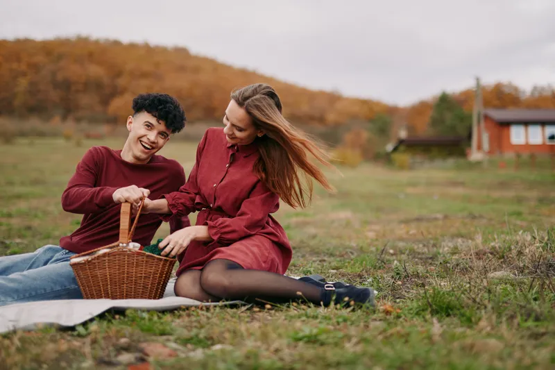A genuine outdoor picnic scene showing an authentic couple sharing a wicker basket on a grassy field, relaxed interaction capturing natural smiles and true connection.