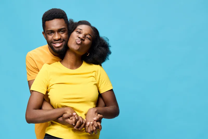 Happy young African couple embracing, wearing bright yellow shirts against a vibrant blue background, showcasing love and joy in a playful manner