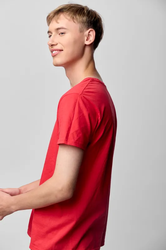 Young man in a red t shirt captured in a clean studio, shown in profile with a relaxed smile, conveying casual style, youthful energy, and approachable fashion for lifestyle visuals