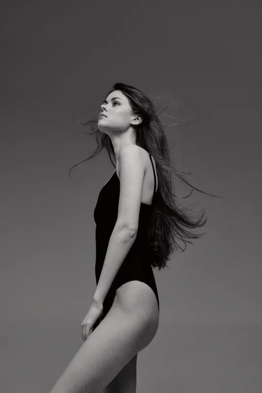Black and white portrait of a woman in a swimsuit with long hair looking upward with a serene expression.