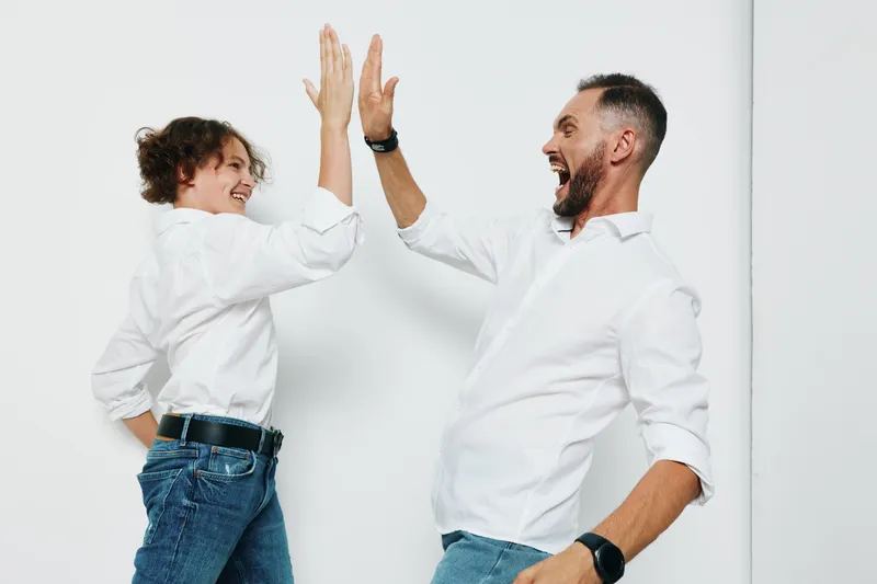 Two business professionals share a high five against an isolated colored backdrop, expressing teamwork, success, and energetic celebration in a modern workplace setting.
