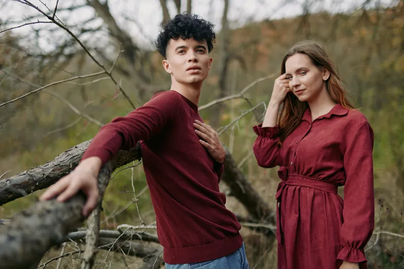 Natural portrait of a young couple in matching burgundy outfits posing outdoors with sincere expressions, capturing authenticity and intimate realism in candid, unposed moments.